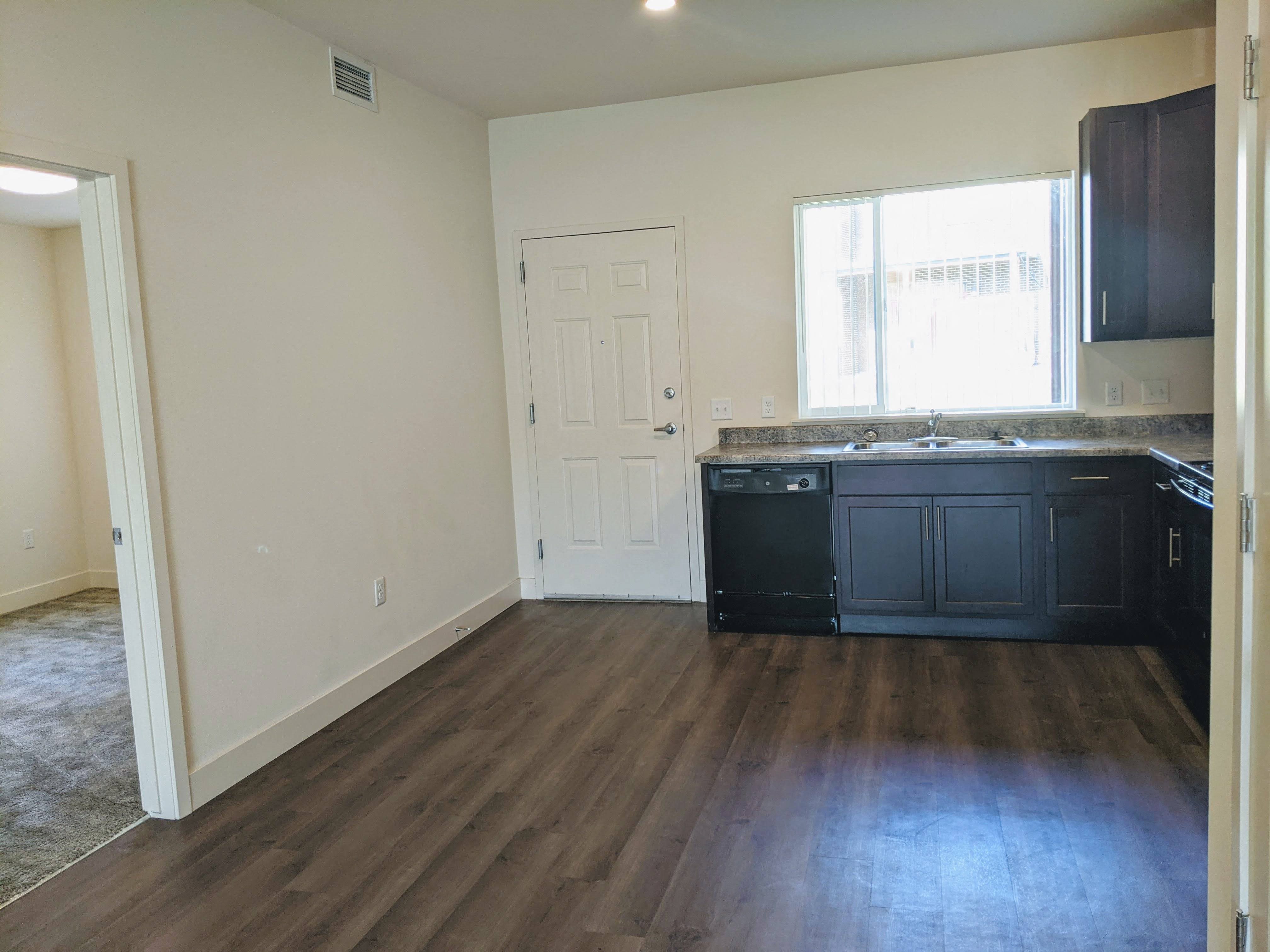 A kitchen next to the front door with a window, dishwasher, sink, and cabinets